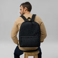 Man on a wooden stool wearing a black backpack gridded with tiny white alchemical symbols